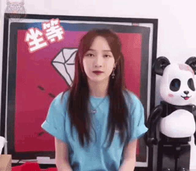 a woman in a blue t-shirt is sitting in front of a panda bear .