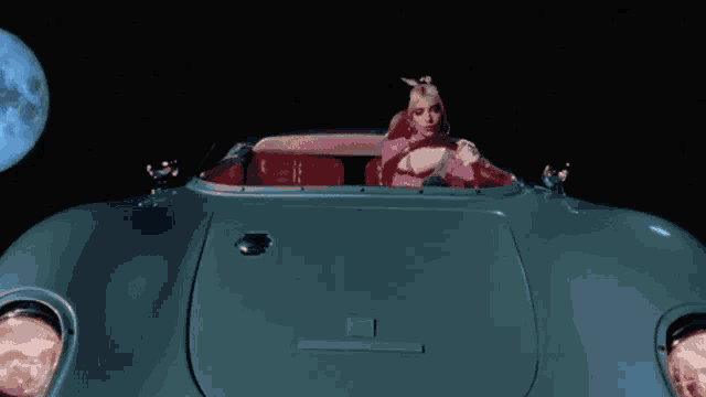 a woman is driving a sports car in front of a full moon .