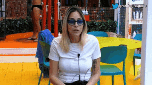 a woman wearing sunglasses and a white shirt is sitting in front of a table .