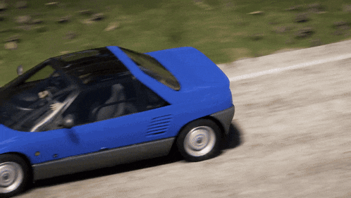 a blue car is driving down a dirt road with grass in the background