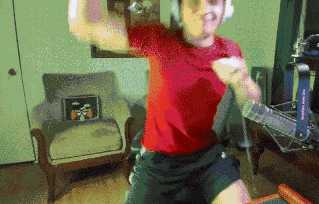 a man in a red shirt is dancing in front of a microphone and chair