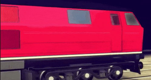 a red train with white wheels is parked on a track .