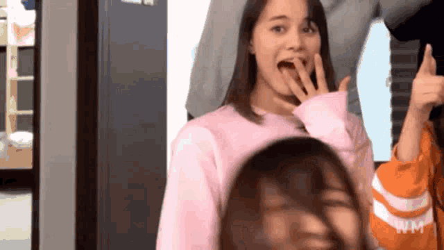 a girl in a pink sweater covering her mouth with her hand