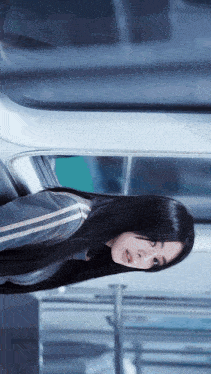 a woman with long black hair looks out of a window