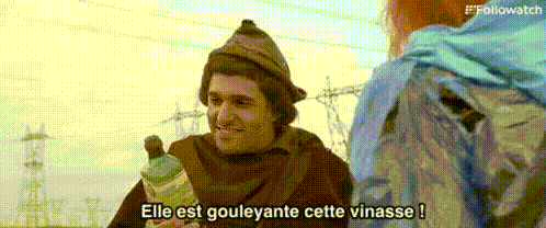 a man in a monk costume is holding a bottle of wine and talking to a woman .