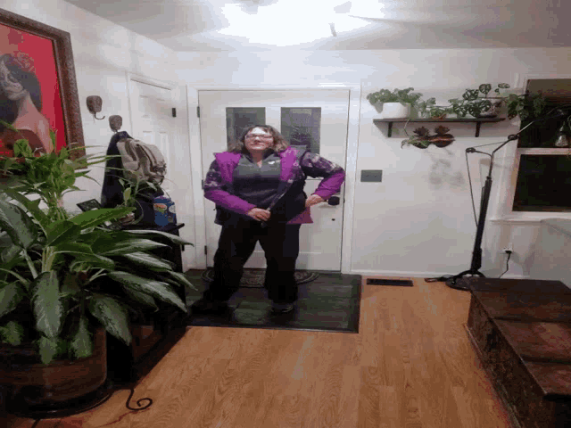 a woman in a purple jacket is standing in a room with plants