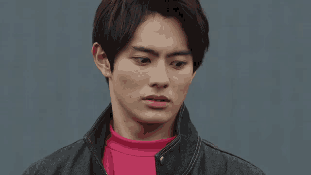 a young man wearing a pink turtleneck and a grey jacket