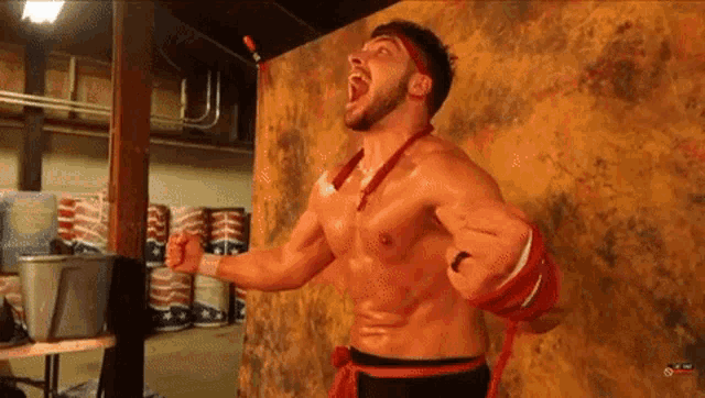a shirtless wrestler is standing in front of a wall with his mouth open .