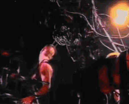 a man is playing a guitar while another man is playing drums in a dark room .