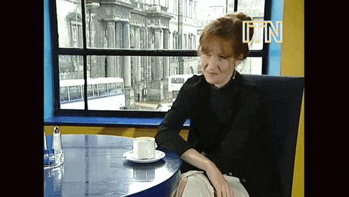 a woman sits at a table with a cup of coffee in front of a window with the letters tn on the wall