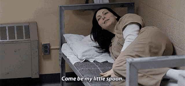 a woman is laying on a bed with the words come be my little spoon written on it .