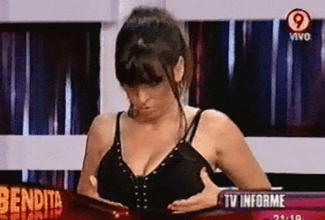 a woman adjusts her bra in front of a sign that says bendita tv informe