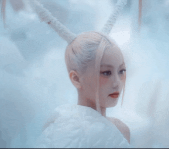 a woman in a white dress with horns on her head looks at the camera