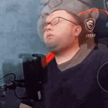 a man wearing glasses is sitting in front of a microphone in a gaming chair .