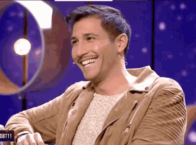 a man in a tan jacket is smiling in front of a sign that says dbt11 on it