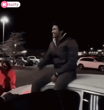 a man is sitting on top of a white car in a parking lot .