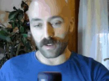 a man with a beard is wearing a blue shirt and looking at a cell phone
