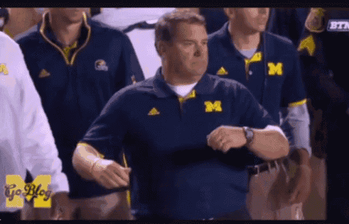a man wearing a blue shirt with the letter m on it looks at his watch