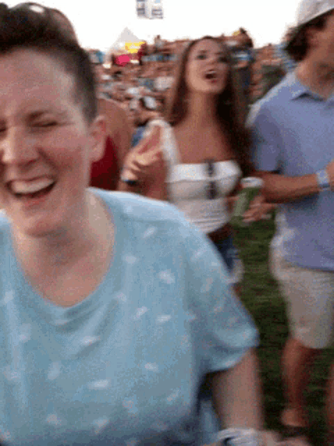 a woman in a blue shirt is laughing while standing in a crowd