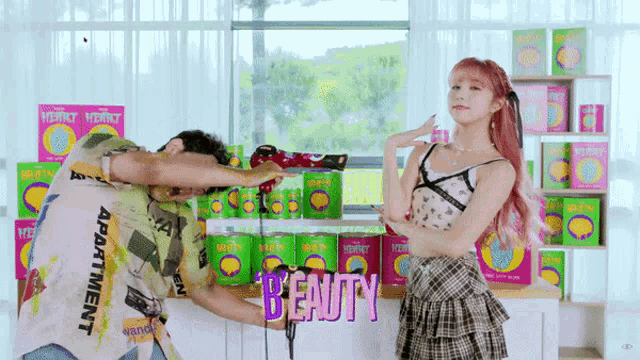 a woman with pink hair is standing next to a man holding a hair dryer in front of a display of beauty products