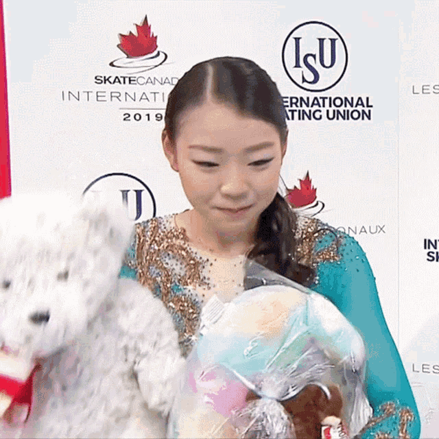 a woman holding a teddy bear in front of a sign that says skate canada international