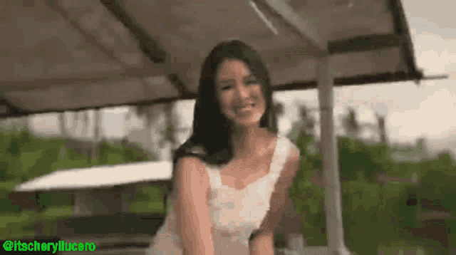 a woman in a white dress is sitting under a canopy and smiling at the camera .