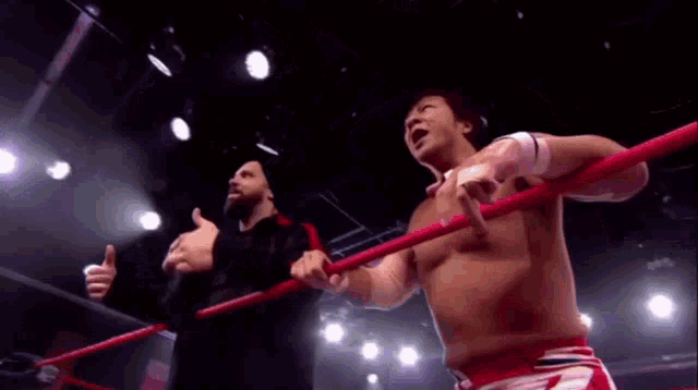 two men are standing in a wrestling ring with their arms outstretched and talking to each other .