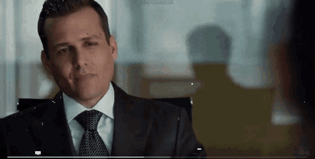 a man in a suit and tie is sitting in a chair and smiling .