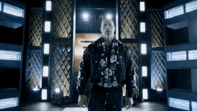 a man in a floral shirt is standing in a dark room with lights behind him