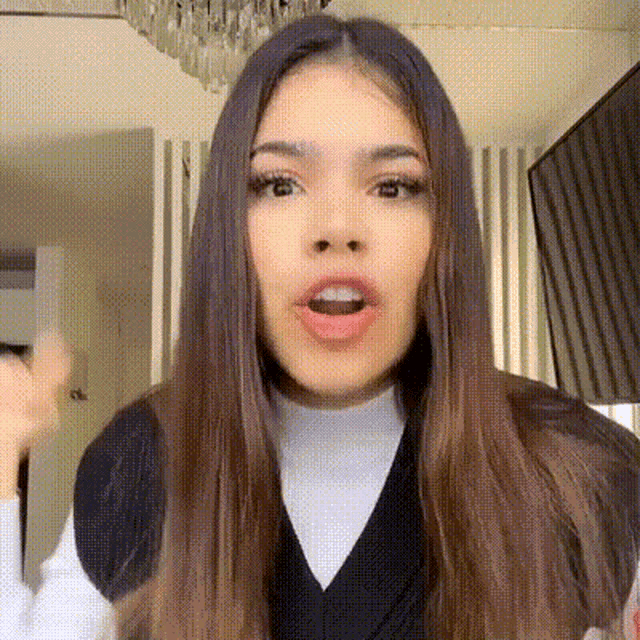 a woman with long hair is making a funny face while wearing a black vest and a white turtleneck .