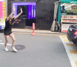 a woman is dancing on the street in front of a store with a sign that says ' korean ' on it