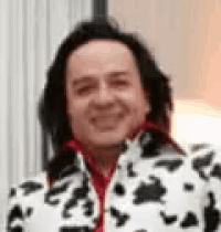 a man with long black hair is wearing a dalmatian print jacket and smiling .