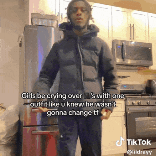 a man in a black jacket stands in a kitchen with a microwave