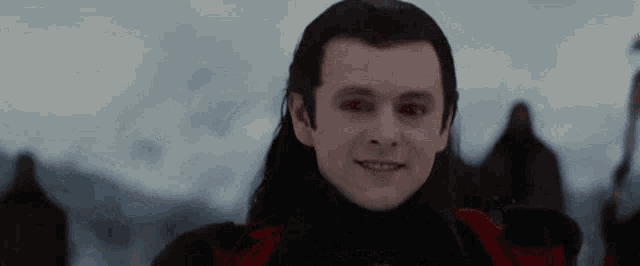 a man with long hair and a red vest is smiling in the snow .