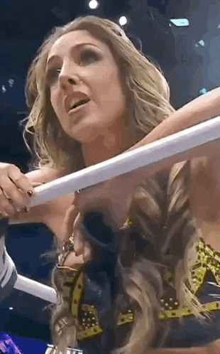 a woman is standing in a wrestling ring holding a rope and looking at the camera .