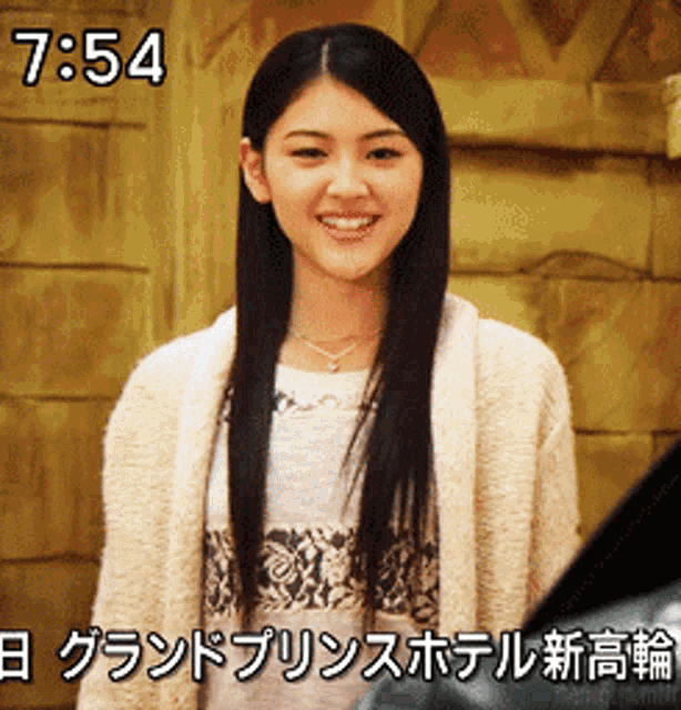 a woman is smiling in front of a wooden wall with the time of 7:54