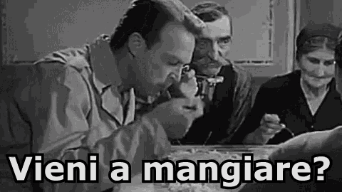 a group of people are sitting at a table eating food with the words vieni a mangiare written above them .
