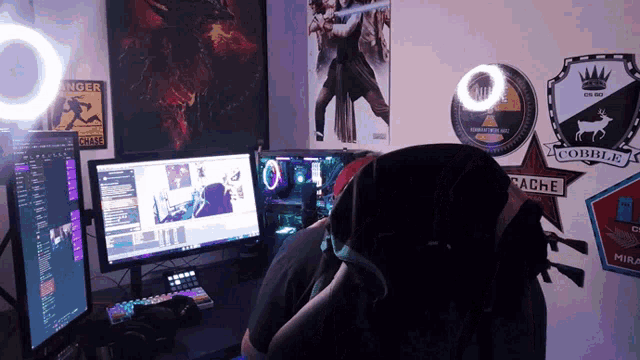 a man sits in front of two computer monitors with a sticker on the wall that says cache