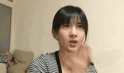 a woman in a striped shirt is making a funny face and waving her hand .