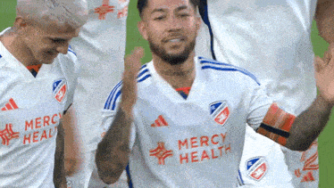 a soccer player wearing a mercy health jersey celebrates with his teammates