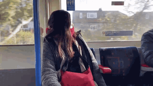 a woman sitting on a bus with a sticker on the window that says please keep two off seats