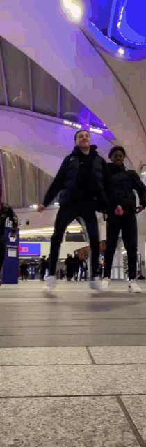two men are jumping in the air while holding hands in a building .