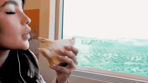 a woman is eating a piece of pizza on a train