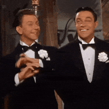 two men in tuxedos are standing next to each other and laughing .