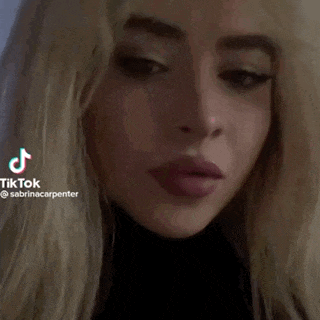 a close up of a woman 's face with a black turtleneck and long blonde hair .