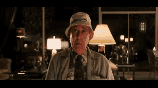 an elderly man wearing a hat and tie is sitting in a living room