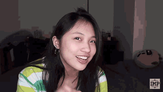 a girl in a green and white striped shirt is smiling in front of a wall that has imp written on it