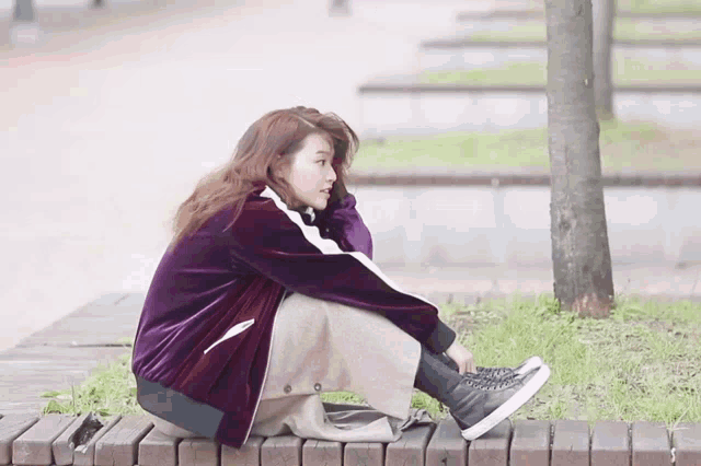 a woman in a purple jacket is sitting on a wooden bench