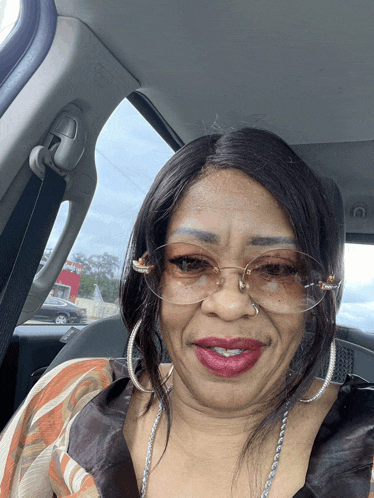 a woman wearing glasses and hoop earrings is smiling in a car