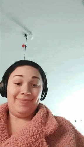 a woman wearing headphones and a pink sweater is smiling and making a funny face .